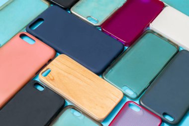 Cep telefonu için çok renkli plastik kapaklar yığını. Mavi arka planda akıllı telefon koruyucusu aksesuarları. Bir sürü silikon telefon ve deri yan yana.