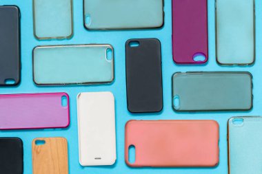 Cep telefonu için çok renkli plastik kapaklar yığını. Mavi arka planda akıllı telefon koruyucusu aksesuarları. Bir sürü silikon telefon ve deri yan yana.