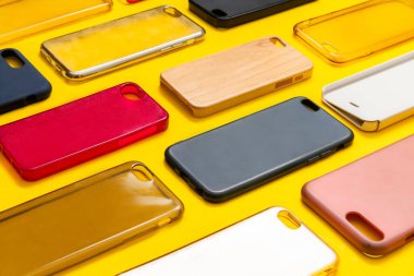 Cep telefonu için çok renkli plastik kapaklar yığını. Sarı arka planda akıllı telefon koruyucusu aksesuarları. Bir sürü silikon telefon ve deri yan yana.