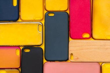 Cep telefonu için çok renkli plastik kapaklar yığını. Sarı arka planda akıllı telefon koruyucusu aksesuarları. Bir sürü silikon telefon ve deri yan yana.