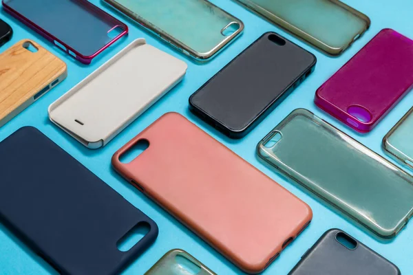 Pile of multicolored plastic back covers for mobile phone. Choice of smart phone protector accessories on blue background. A lot of silicone phone backs or skins next to each other