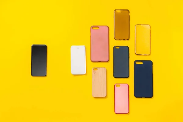 Pile of multicolored plastic back covers for mobile phone on yellow background. Choice of smart phone protector accessories. A lot of silicone phone backs or skins next to smart phone