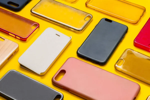 Pile of multicolored plastic back covers for mobile phone. Choice of smart phone protector accessories on yellow background. A lot of silicone phone backs or skins next to each other