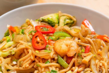 Karidesli, brokolili, ahşap bir tabakta kırmızı biberli baharatlı deniz ürünü şehriye.