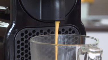 Kapsül makinesinin ferahlatıcı espresso 'sunu evdeki bir bardağa boşalt. Kahve molası kavramı. 
