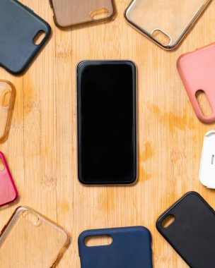 Ahşap arka planda cep telefonları için çok renkli plastik kapaklar ve yanında da bir telefon var.