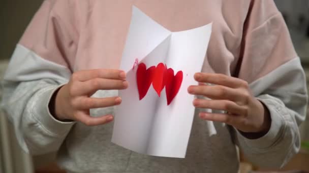 バレンタインデーに手作りグリーティングカードを展開する手 白い紙に赤いペンキでペイントしたサインが好き — ストック動画