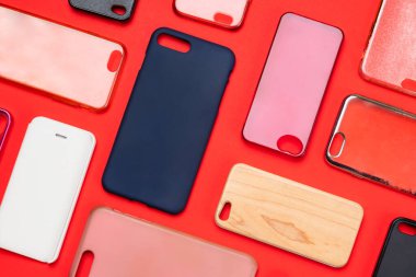 Cep telefonu için çok renkli plastik kapaklar yığını. Kırmızı arka planda akıllı telefon koruyucusu aksesuarları. Bir sürü silikon telefon ve deri yan yana.