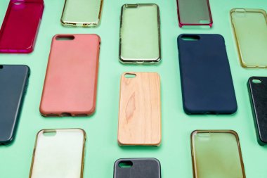 Cep telefonu için çok renkli plastik kapaklar yığını. Yeşil arka planda akıllı telefon koruyucusu aksesuarları. Bir sürü silikon telefon ve deri yan yana.