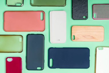 Cep telefonu için çok renkli plastik kapaklar yığını. Yeşil arka planda akıllı telefon koruyucusu aksesuarları. Bir sürü silikon telefon ve deri yan yana.
