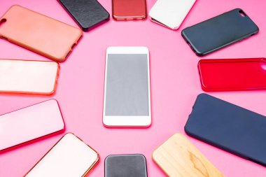 Pembe arka planda cep telefonları için çok renkli plastik arka kapaklar ve yanında akıllı bir telefon seçeneği.