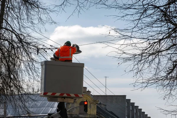 Güneşli bir günde asansör platformunda koruyucu iş kıyafetleri giyen elektrikçi sokak lambalarını değiştiriyor..