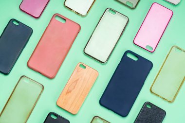 Cep telefonu için çok renkli plastik kapaklar yığını. Yeşil arka planda akıllı telefon koruyucusu aksesuarları. Bir sürü silikon telefon ve deri yan yana.