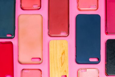 Cep telefonu için çok renkli plastik kapaklar yığını. Pembe arka planda akıllı telefon koruyucusu aksesuarları. Bir sürü silikon telefon ve deri yan yana.