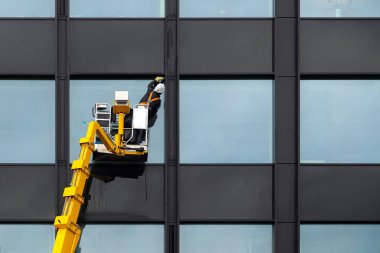 Modern binaların cam temizleyicisi, asansör platformunda havada asılı duran erkek. Havada cam parlatan işçiler.