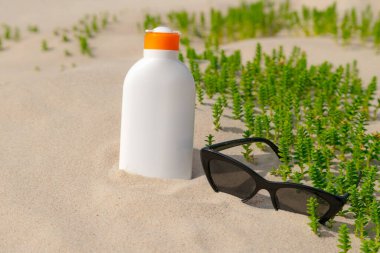Güneşli bir günde kumsalda güneş kremi ve güneş gözlüğü. Güneş yanığından korunan beyaz güneş kremi şişesi. Kimse..