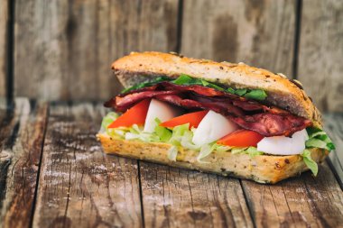 Yumurta, domates, marul ile pastırma baget. Üzerinde eski bir ahşap masa.