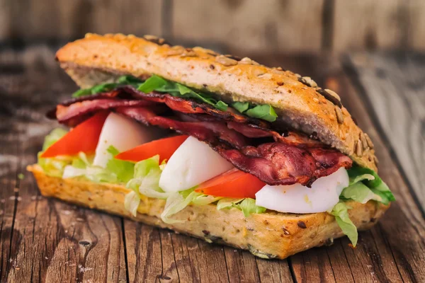 Speckbaguette mit Ei, Tomate und Salat. auf einem alten Holztisch. — Stockfoto