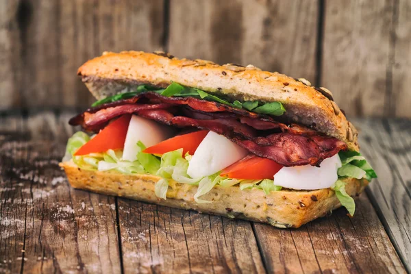 Speckbaguette mit Ei, Tomate und Salat. auf einem alten Holztisch. — Stockfoto