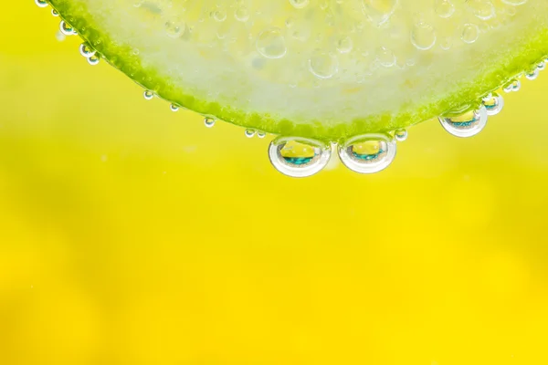 Green lime with water splash. Yellow background. — Stock Fotó