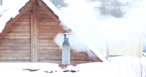 O fumo vem da chaminé da casa, da casa de banho, do rebanho. Edifício de neve e telhado. — Vídeo de Stock