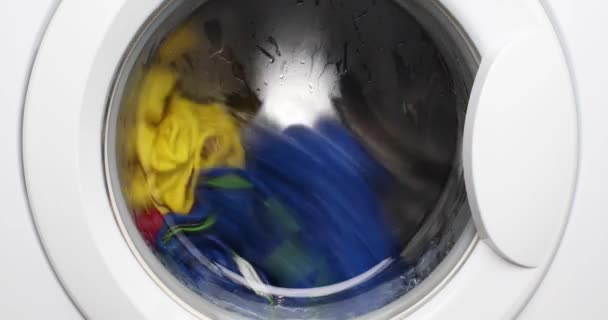 Kapalı beyaz çamaşır makinesi çok renkli tişörtler yıkıyor, kırmızı, sarı ve mavi.. — Stok video