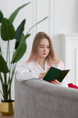 Sarışın, beyaz saçlı, iş kadını. Not defterine, günlüğüne, planlama işine ve ilişki programına yazıyor. Kanepede oturuyor, dikey çekim yapıyor, ofis tarzında..