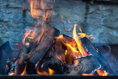 Taş bir duvarın arkasında yanan barbekü şenliği ateşi.