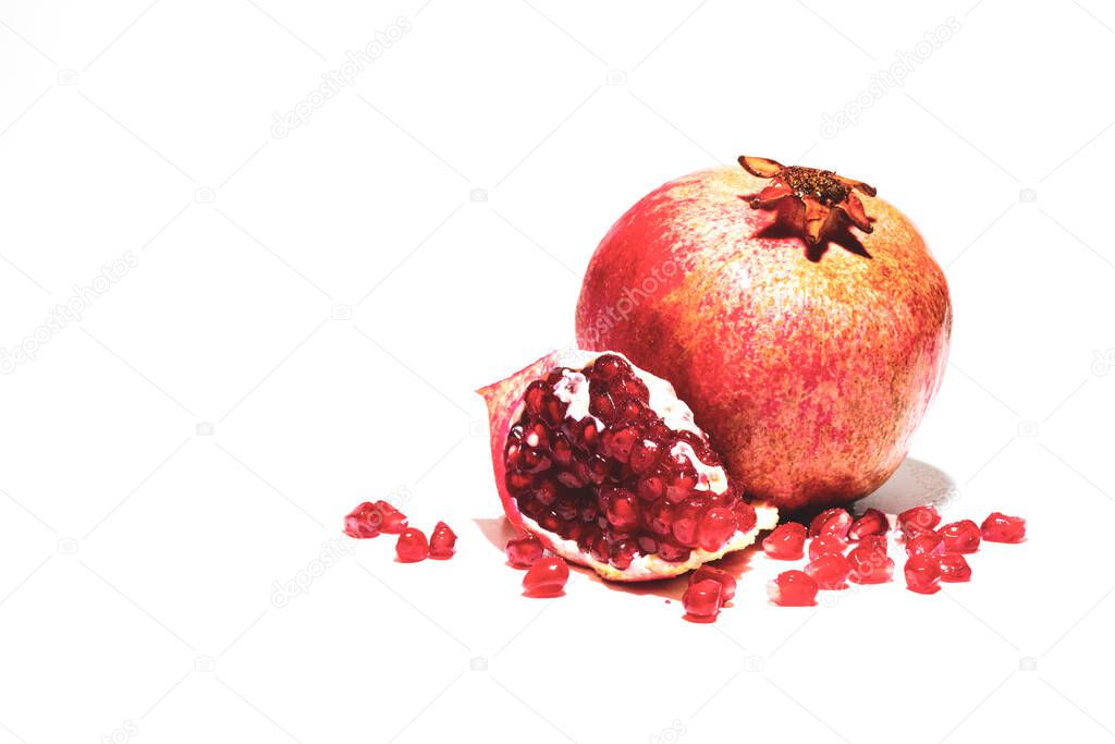 One ripe red pomegranate and a piece of pomegranate with grains on a white background