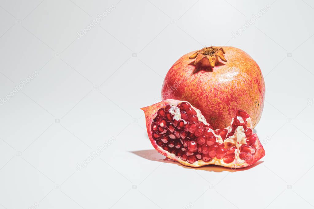 Ripe red pomegranate and piece of pomegranate with grains on a white background