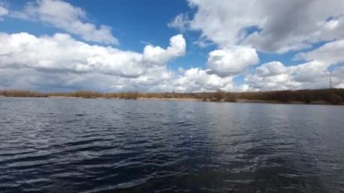 Nehirde küçük dalgalar halinde büyük bulutların arka planına doğru hareket ediyorlar. Bahar manzarası