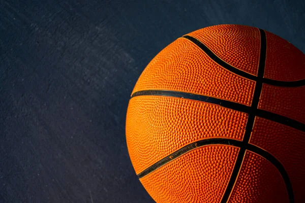 Koyu beton zeminde güneş ışığıyla aydınlatılan bir basketbol topu. Seçici odak.