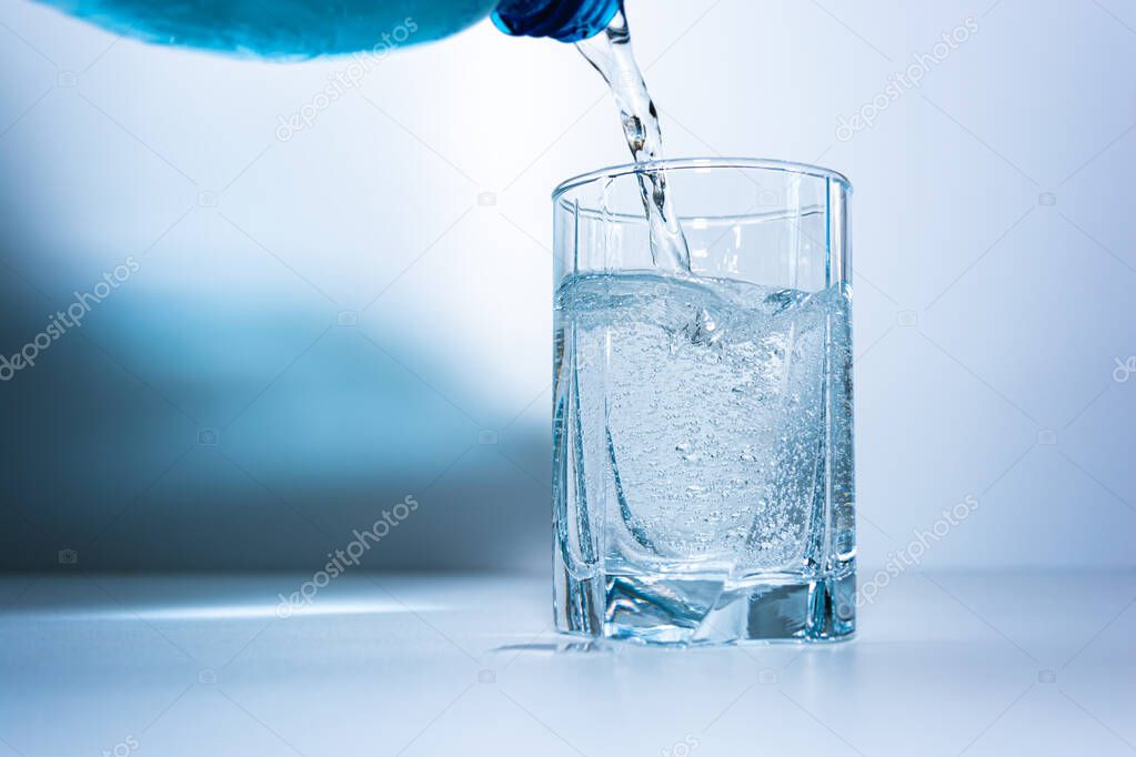 Pouring mineral water into a glass beaker. The photo shows part of a plastic bottle and an almost full glass of water with gas bubbles.