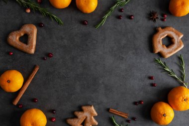 Noel ve yeni yıl arkaplanı zencefilli ekmek, mandalina, biberiye ve koyu gri arka planda kızılcık. Üst manzara, düz yatak, Noel yemeği dekorasyonu. Tebrik kartı için festival çerçevesi kavramı