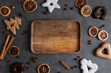 Ortasında tahta tepsi olan Noel tatili sınır arkaplanı. op view, flat lay, fotokopi alanı, koyu gri arka planda noel ve yeni yıl yemekleri dekorasyonu. Tatil tebrik kartı.