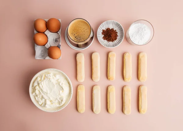 Ingredients for tiramisu at pink minimal background. Savoiardi, cream cheese, eggs, coffee espresso, cocoa and powdered sugar at pink.