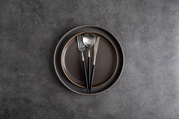Стол с тарелками и столовыми приборами на сером фоне. Вид сверху, плоская лежанка, концепция накрытия темного стола. Копирование текста