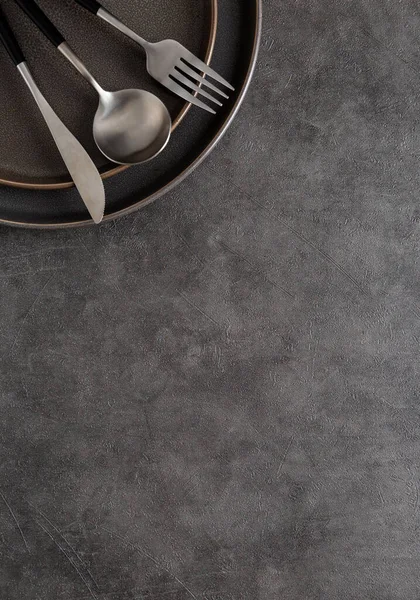 Fork, spoon and knife on dark round ceramic plate on dark gray concrete background with copy space. Top down view, flat lay, place for text, template — Stock Image Fork Spoon Knife Dark Ceramic Plate Dark Gray Concrete Background Stock Image
