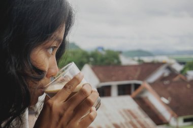 Endonezyalı kız balkonda kahve içiyor.