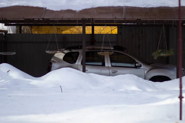 The car is under a canopy behind a thick layer of white snow