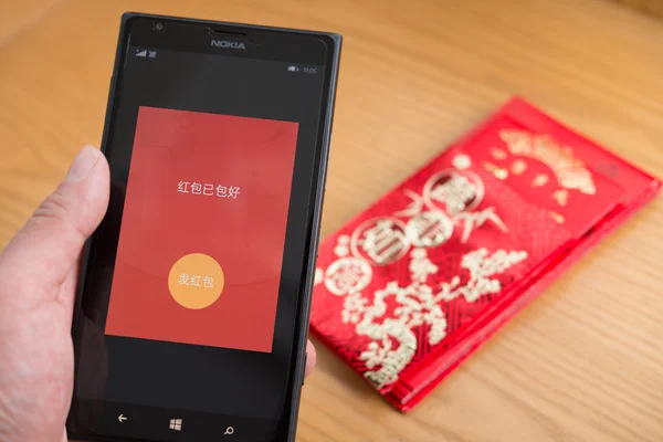 Zhongshan, China-Fev 21,2016: um bolso vermelho no celular está pronto para ser enviado no WeChat para o ano novo chinês com bolsos vermelhos reais no fundo. FEB 8 é o primeiro dia do ano do macaco e envio de receber bolsos vermelhos on-line é muito popular na China . — Fotografia de Stock