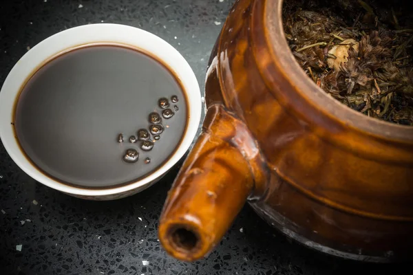 Bowl of Chinese herbal tea and an enamel pot with herbs nearby — Stock Photo, Image