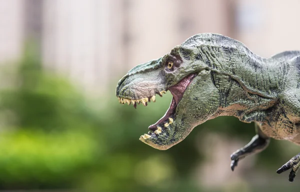 Tyrannosaurus toy in front of trees and a morden building — Stock Photo, Image
