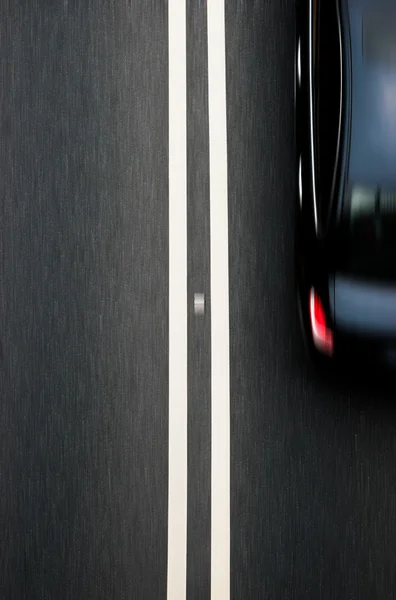 Doppelter weißer Linienteiler auf Blacktop mit einem vorbeifahrenden Auto — Stockfoto