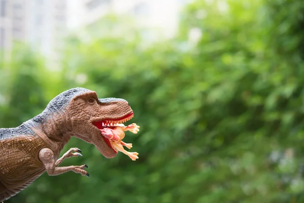 Gigantic tyrannosaurus catches a smaller dinosaur in front of trees and building — Stock Photo, Image