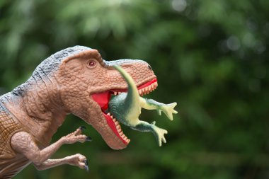 devasa tyrannosaurus ağaçların önünde küçük bir dinozor yakalar