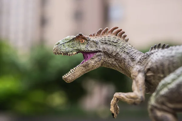Аллозавр игрушка стоит перед деревьями и здания — стоковое фото