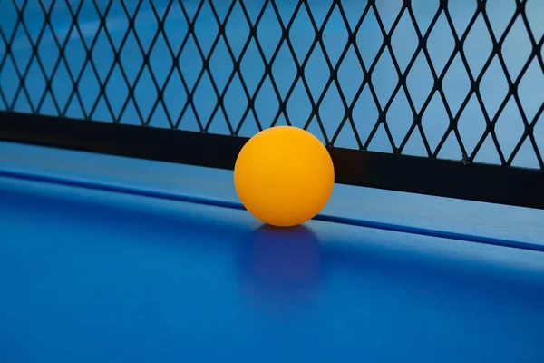 Boule jaune frappe le fond du filet sur une table de pingpong bleu fermer — Photo