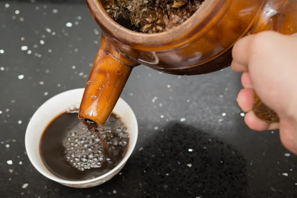 Kräutertee aus einer Emaille-Kanne mit Kräutern in eine Schüssel gießen — Stockfoto