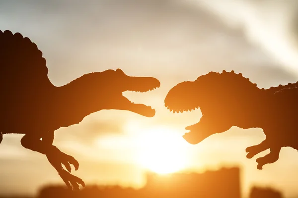 Silhouette of spinosaurus and tyrannosaurus with buildings in far end in sunset time — Stock Photo, Image